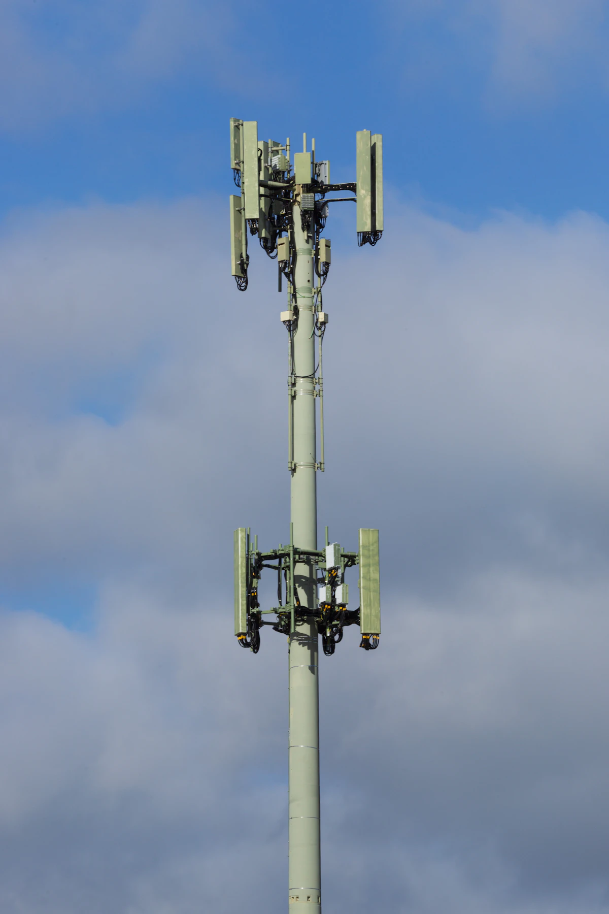 Telecom tower with cellular antennas against a cloudy sky.